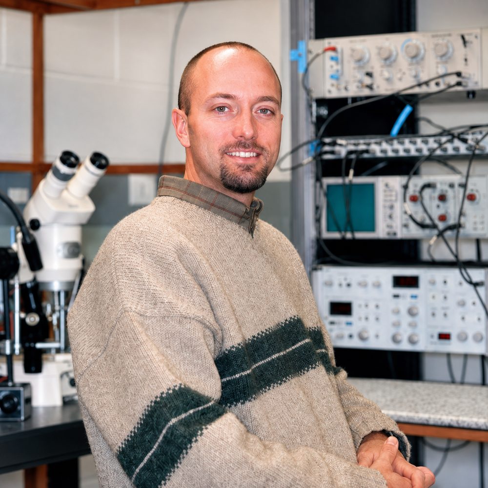 Tim Fergestad at an electrophysiology rig, with a microscope and signal amplifiers