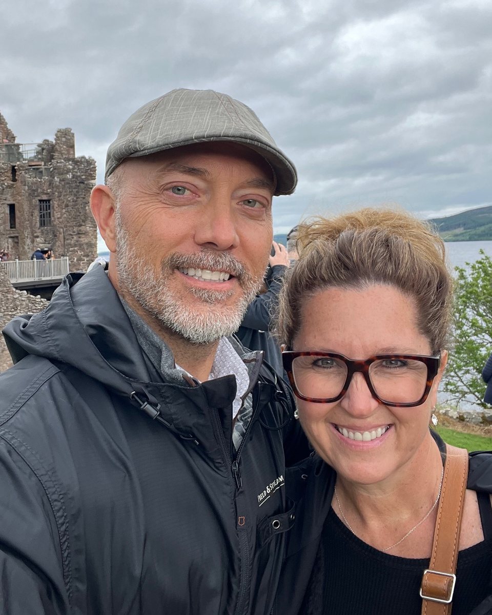 Tim and his wife smiling at Urquhart Castle, with the ruins and Loch Ness behind them